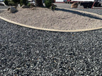 Black n Silver Rock 1 inch surrounding a curbed planter island with palm and boulders